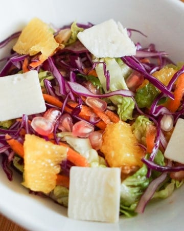 Winer salad with lettuce, cabbage carrot, pomegranate, orange and cheese in a white bowl.