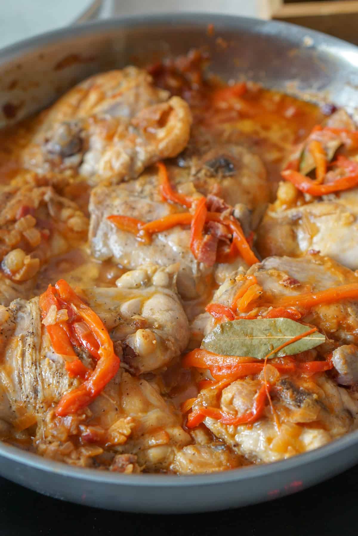 Chicken chilindron in a stainless steel skillet. An overhead photo of chicken thighs in a red sauce with onion and strips of bell pepper.