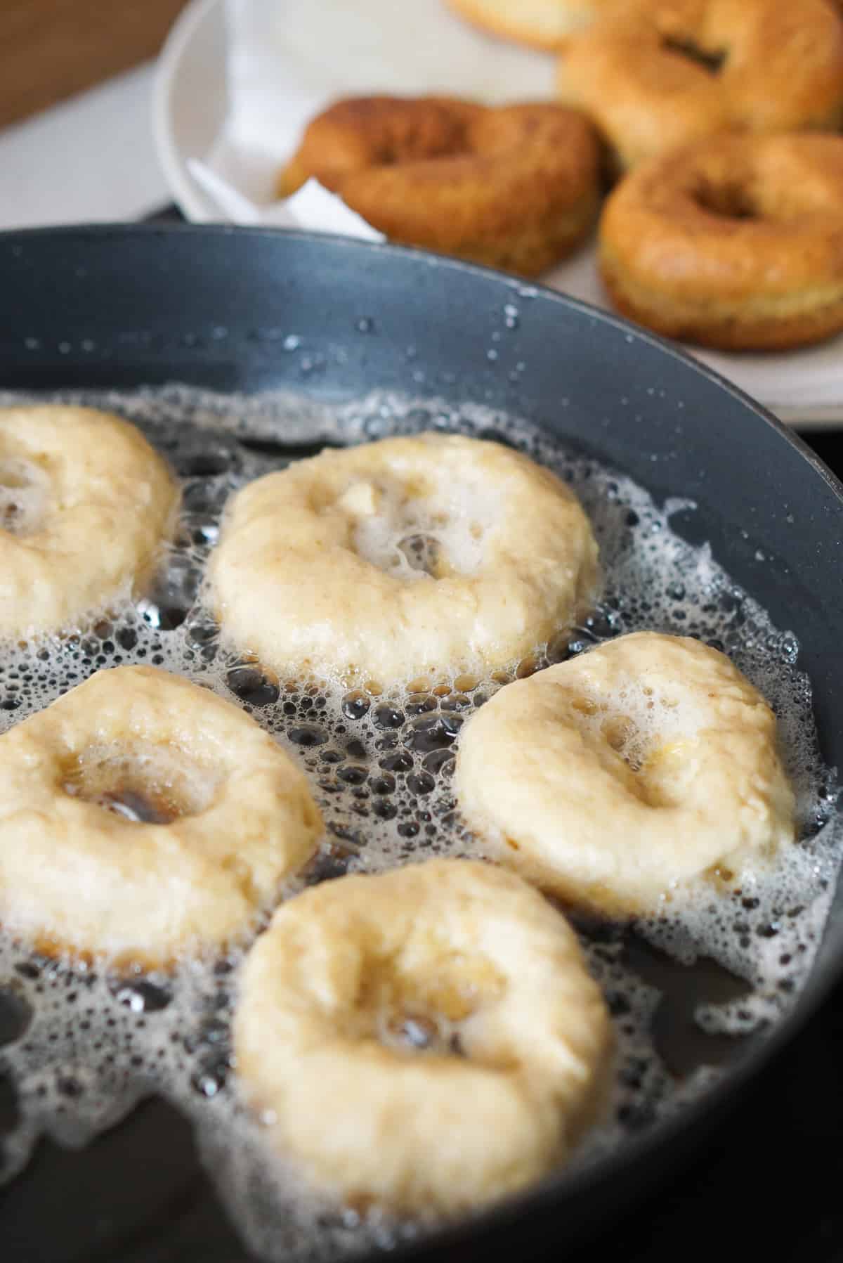Donuts frying in a cast iron skillet.