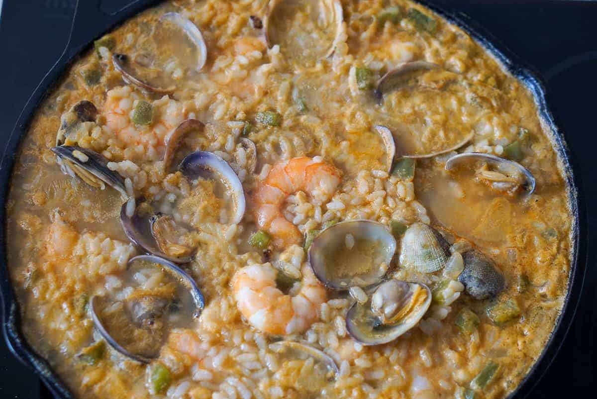 Soupy seafood rice with clams and shrimp in a cast iron pan.