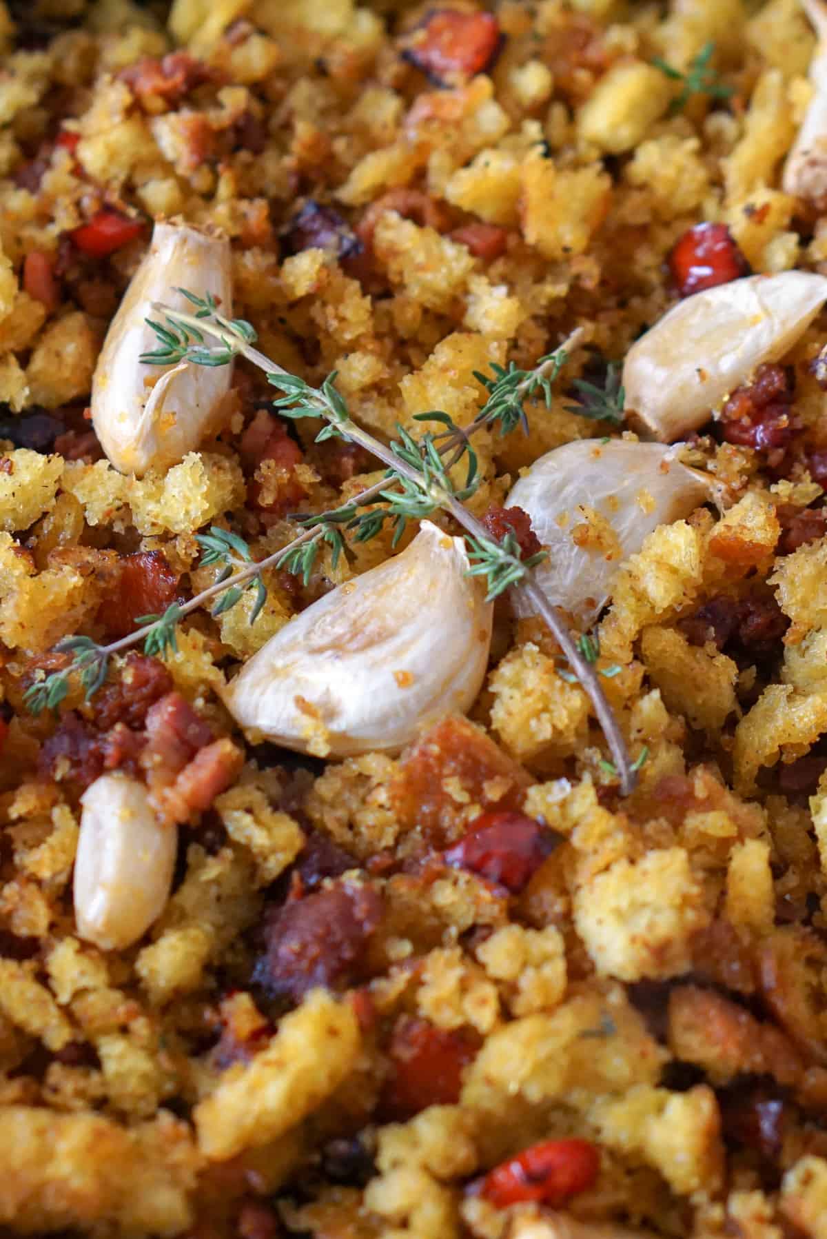 Vertical photo of migas con chorizo, golden fried bread crumbs with chorizo sausage and whole garlic cloves and rosemary on top.