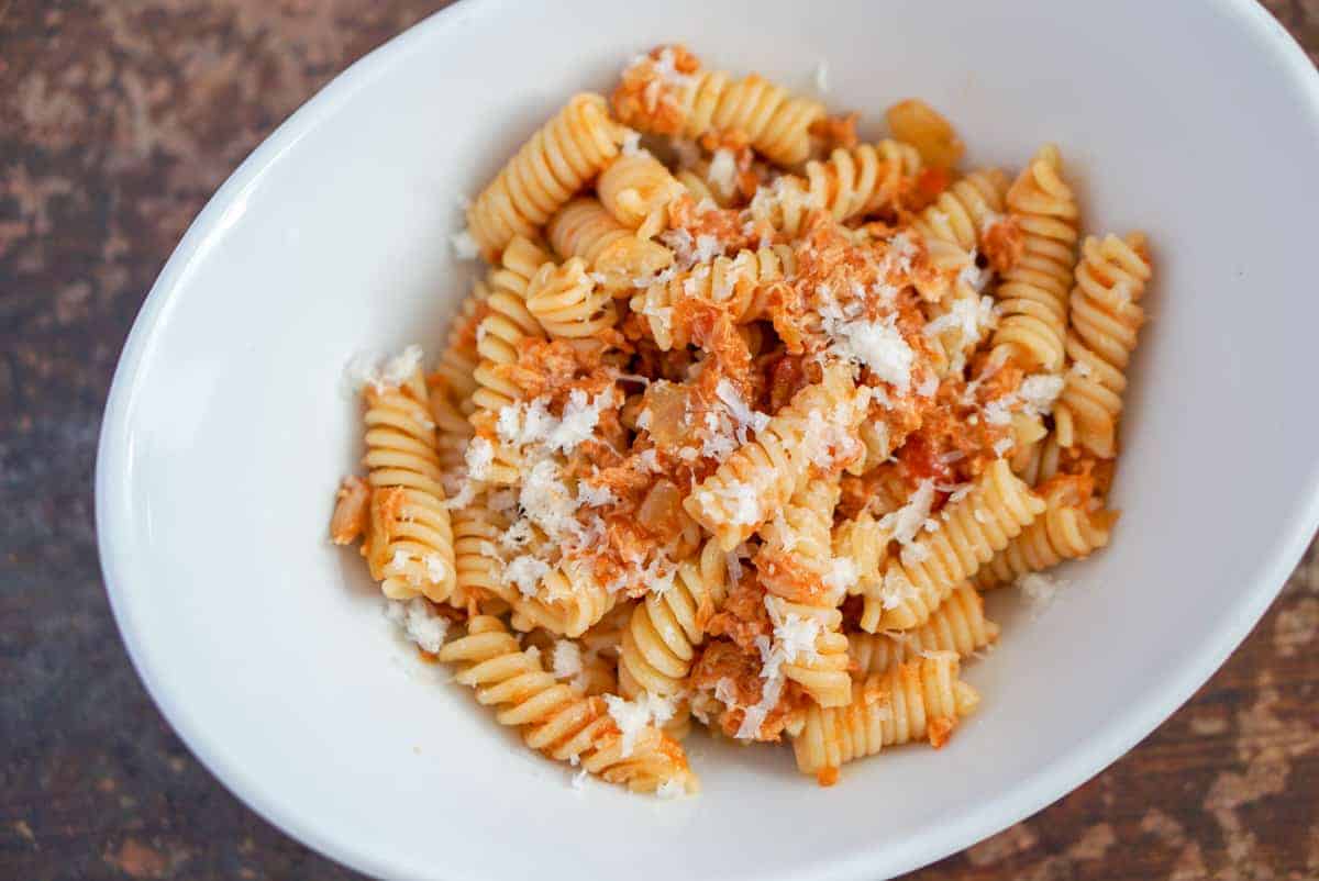 Pasta with grated Manchego cheese and Spanish canned tuna in a white bowl.