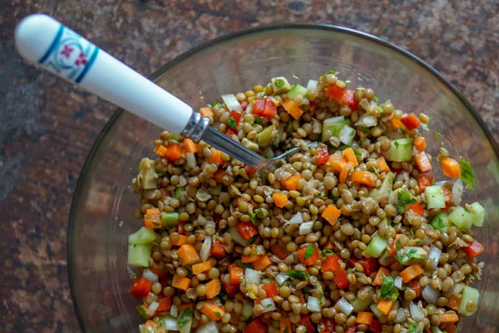 Lentil salad in a clear bowl with a serving spoon