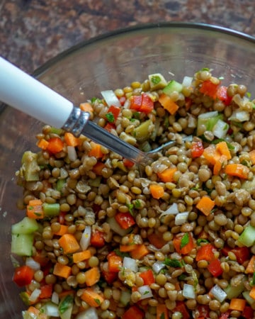 Lentil salad in a clear bowl with a serving spoon