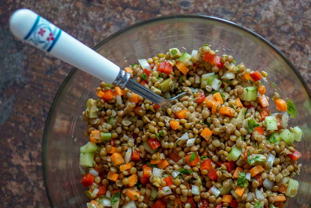 Lentil salad in a clear bowl with a serving spoon