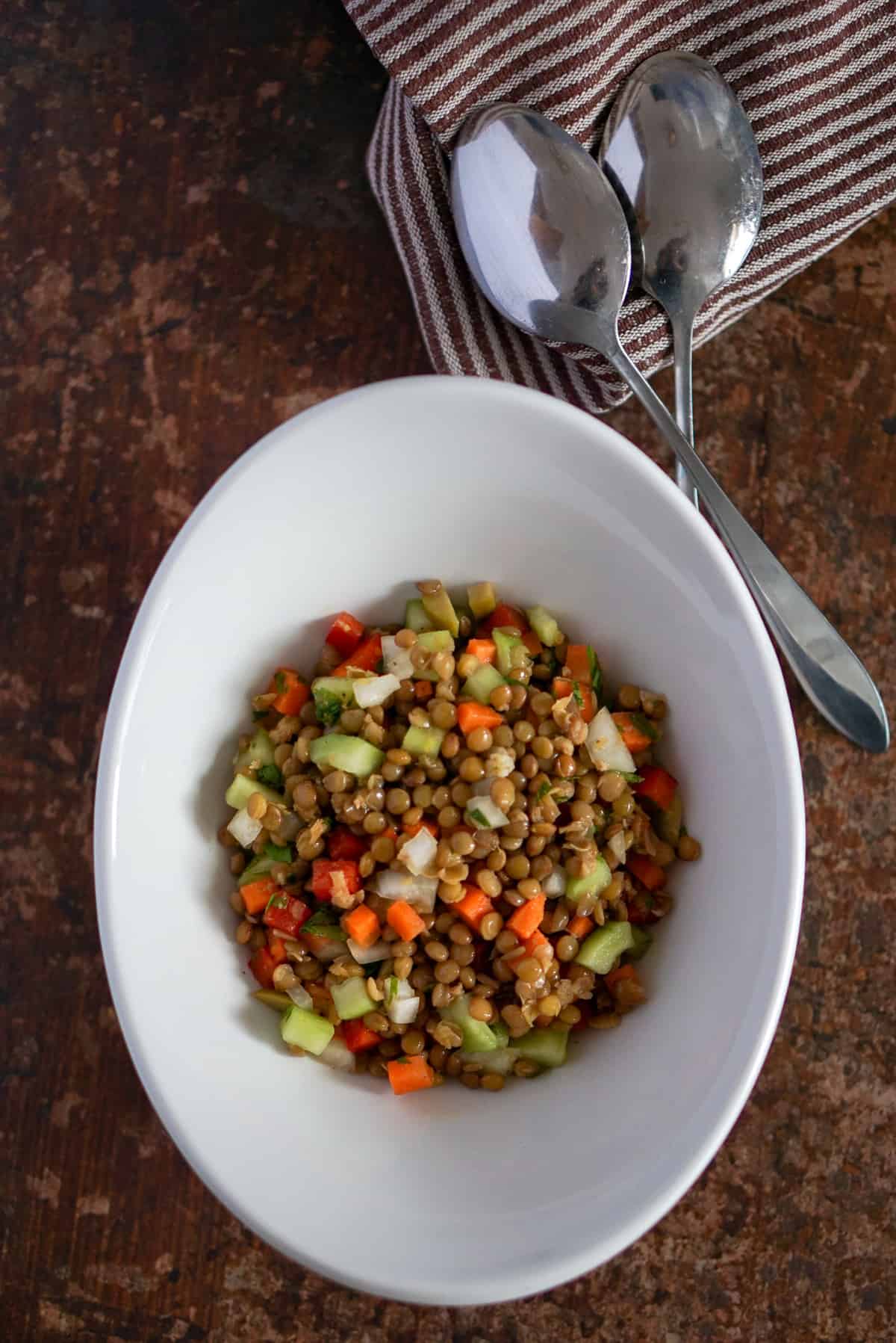 Lentil salad in a white bowl with two serving spoons