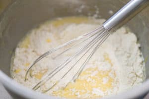 Adding dry ingredients to wet cake batter in a metal bowl with a whisk.