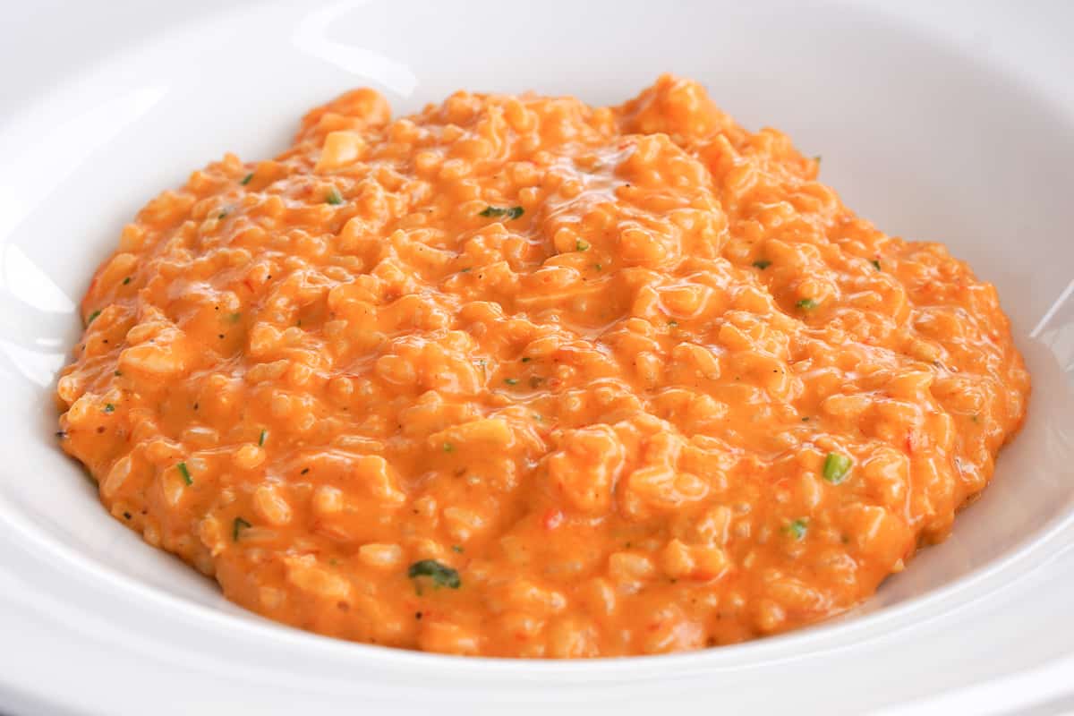 Creamy bright orange rice speckled with green, in a white bowl.