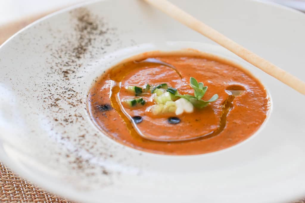 Vegetable gazpacho with toppings and olive oil in a large white bowl.