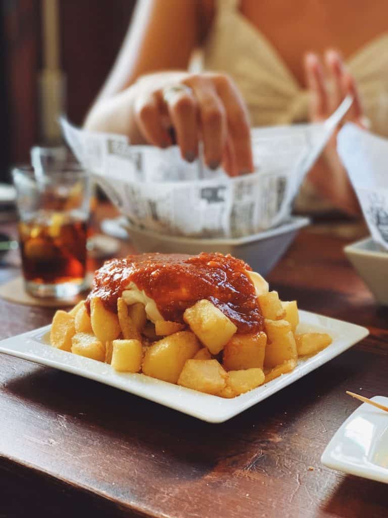 Plate of patatas bravas on a restaurant table with other dishes in the background.