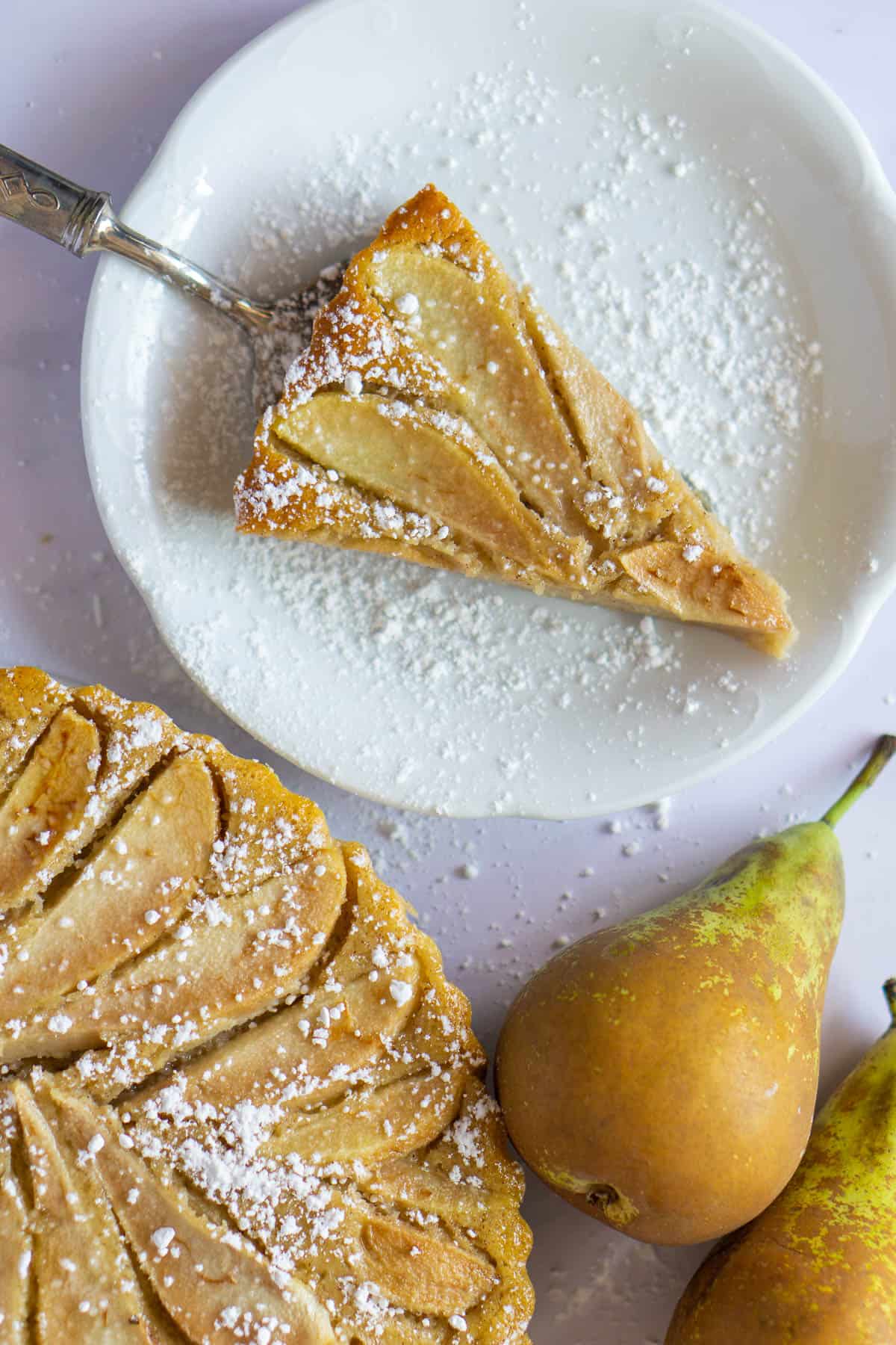 Pear tart slice on a white dish with powdered sugar sprinkled on top.