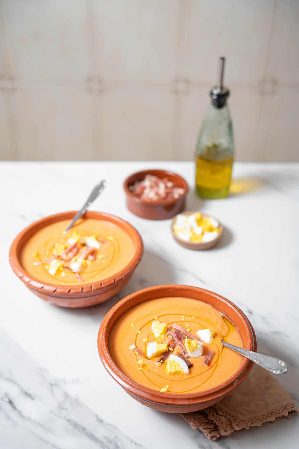 two bowls of salmorejo with a bottle of olive oil.