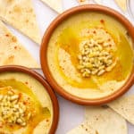 Two clay tapas dishes filled with hummus with pine nuts and paprika.