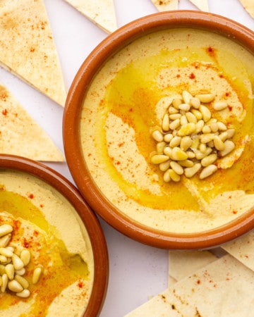 Two clay tapas dishes filled with hummus with pine nuts and paprika.