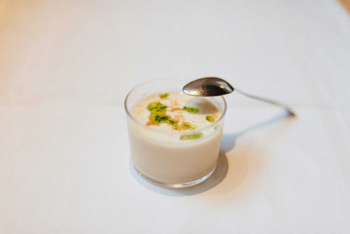 Cold garlic soup in a small clear glass garnished with bright green sauce.