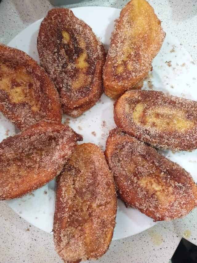 7 slices of French toast made with a baguette dusted in cinnamon sugar and arranged on a plate.