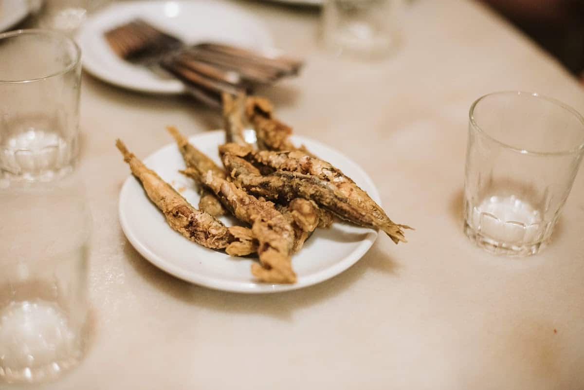 A small plate of fried anchovies next to a few empty glasses.