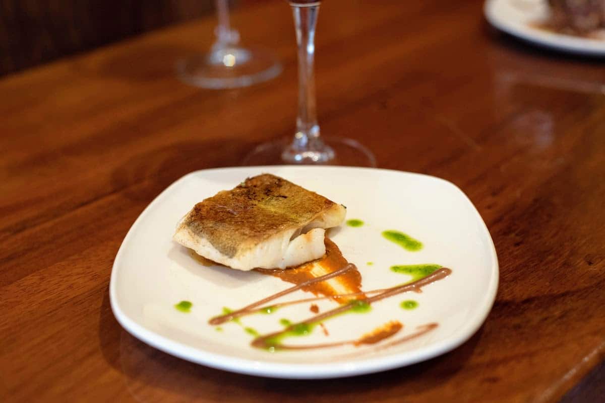 Modern presentation of a cod fillet on a bed of dark orange romesco sauce.