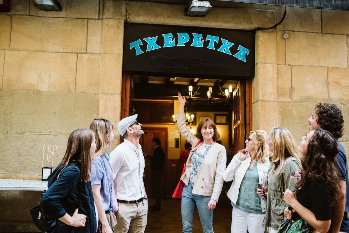 Group of people outside a bar named Txepetxa, written in blue lettering on a black background.