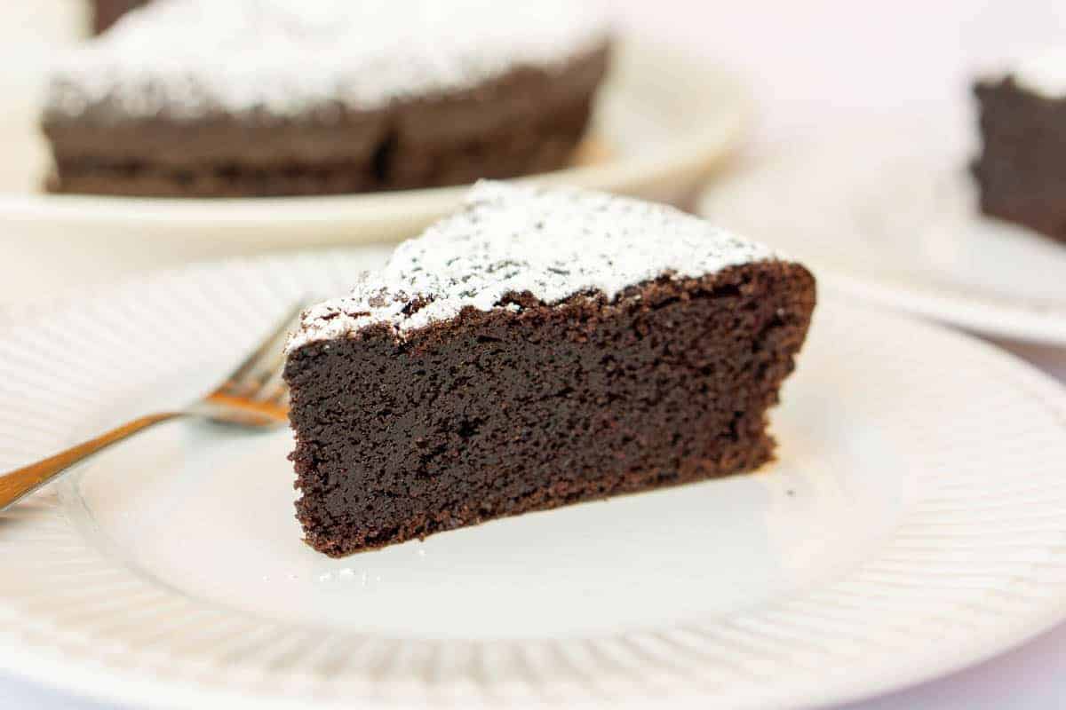 A slice of chocolate olive oil cake topped with powdered sugar on a white plate.