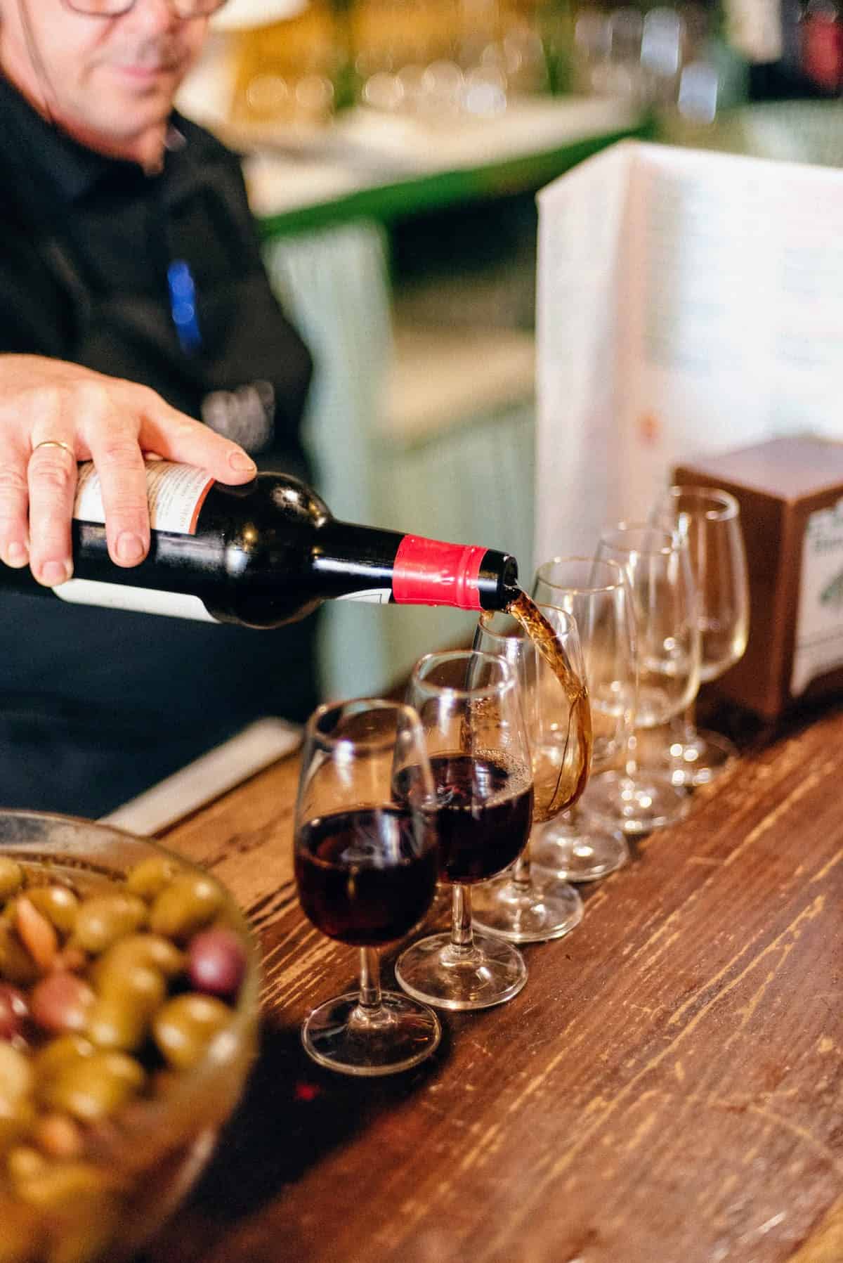 Bartender pouring several glasses of dark brown sherry wine on a wooden bar top