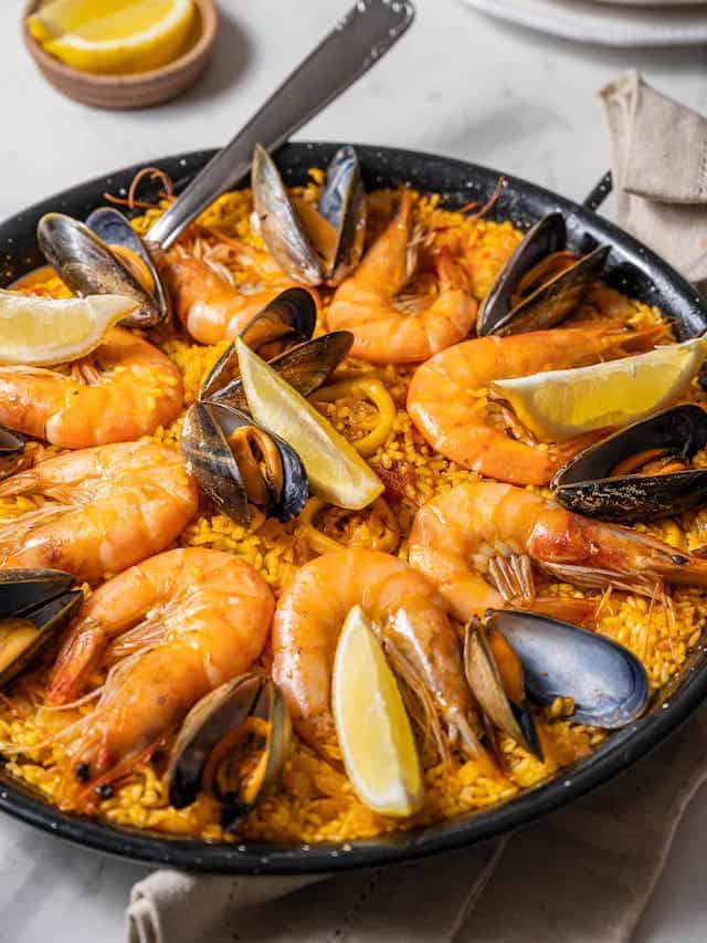 Pan of seafood paella topped with jumbo shrimp, mussels, and lemon slices.