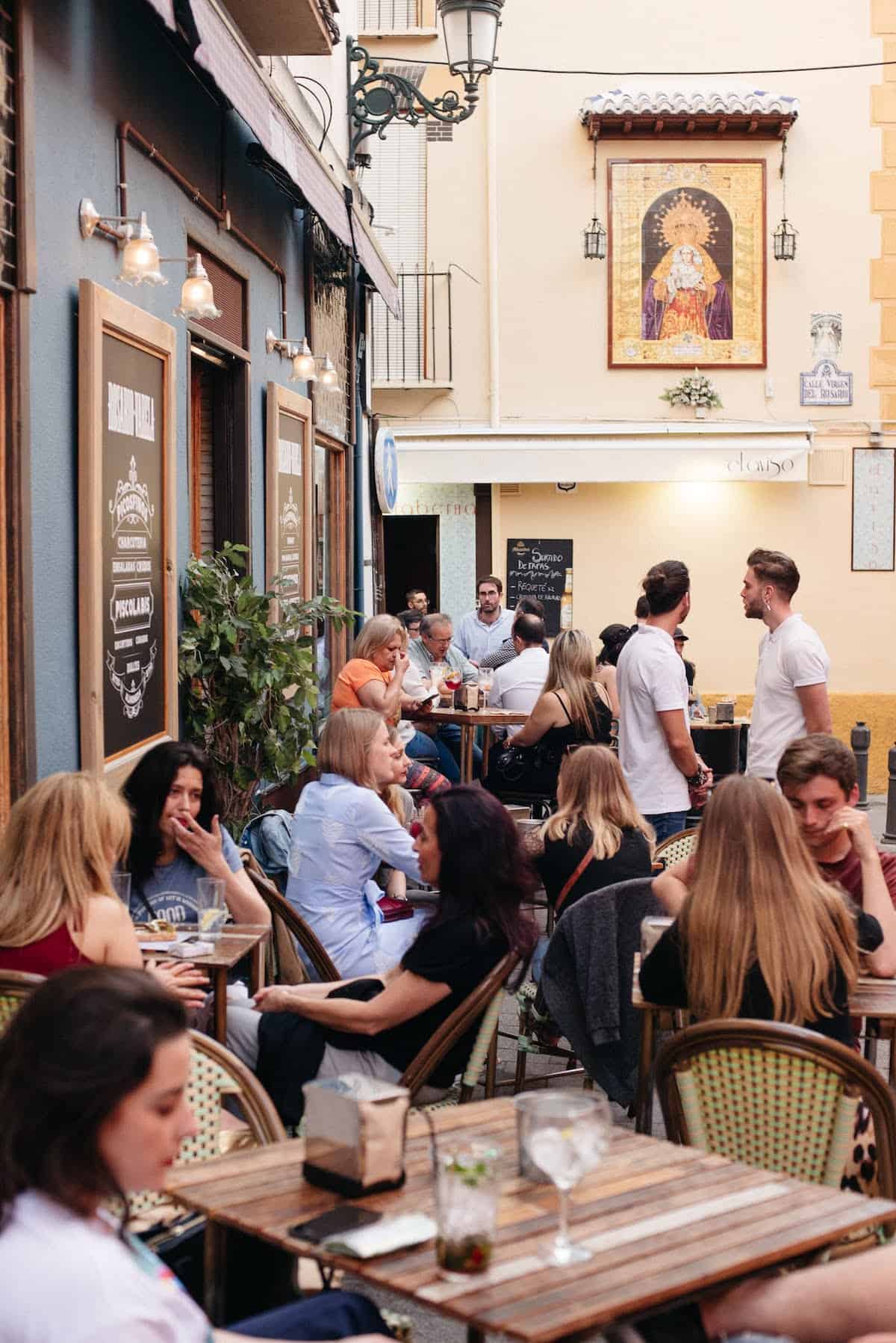 People eating and drinking on a crowded outdoor terrace outside a bar.