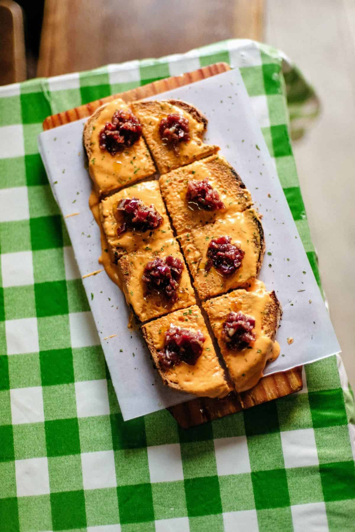 Overhead shot of toasted bread topped with chilled tomato puree and diced ham, against a green and white checkered tablecloth