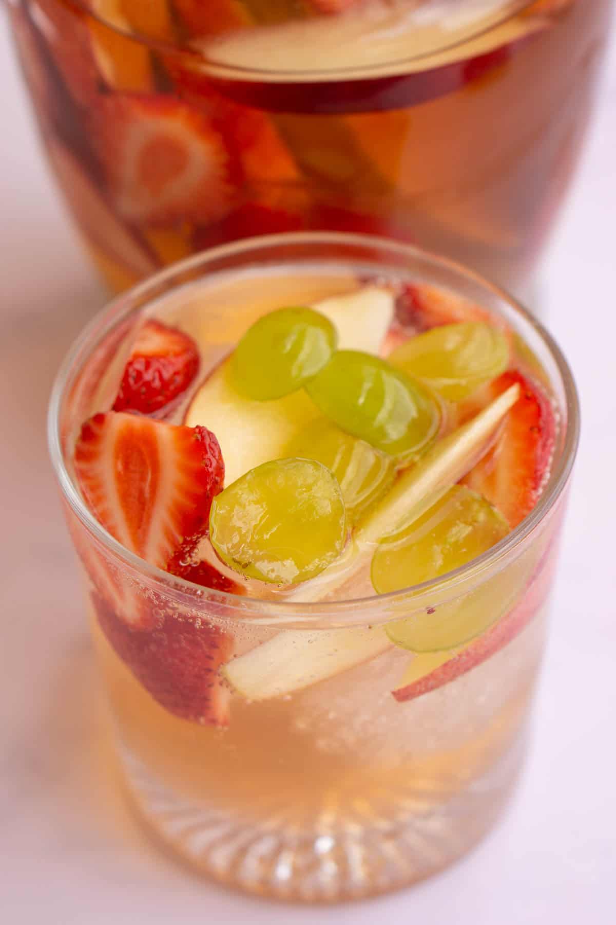 Glass of white wine sangria filled with apple, nectarine, grapes, strawberries and ice.