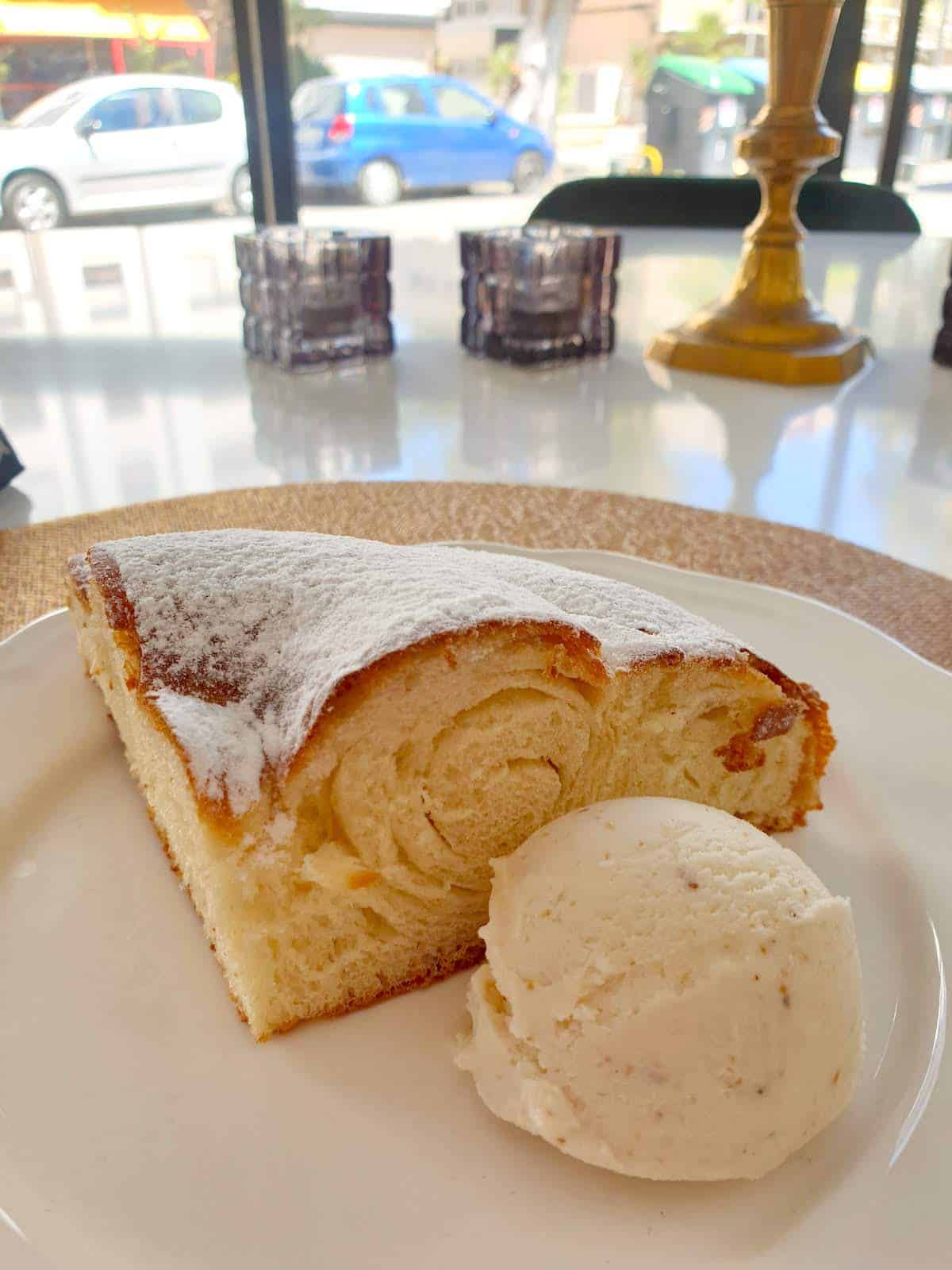 Pastry covered in powdered sugar on a white plate beside a scoop of vanilla ice cream.