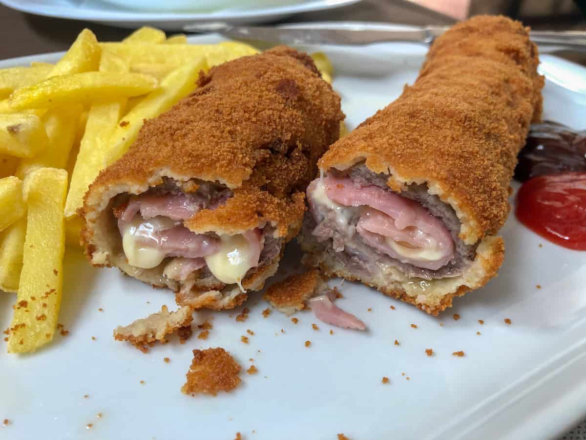 Fried pork rolls stuffed with cheese on a white plate next to a pile of french fries
