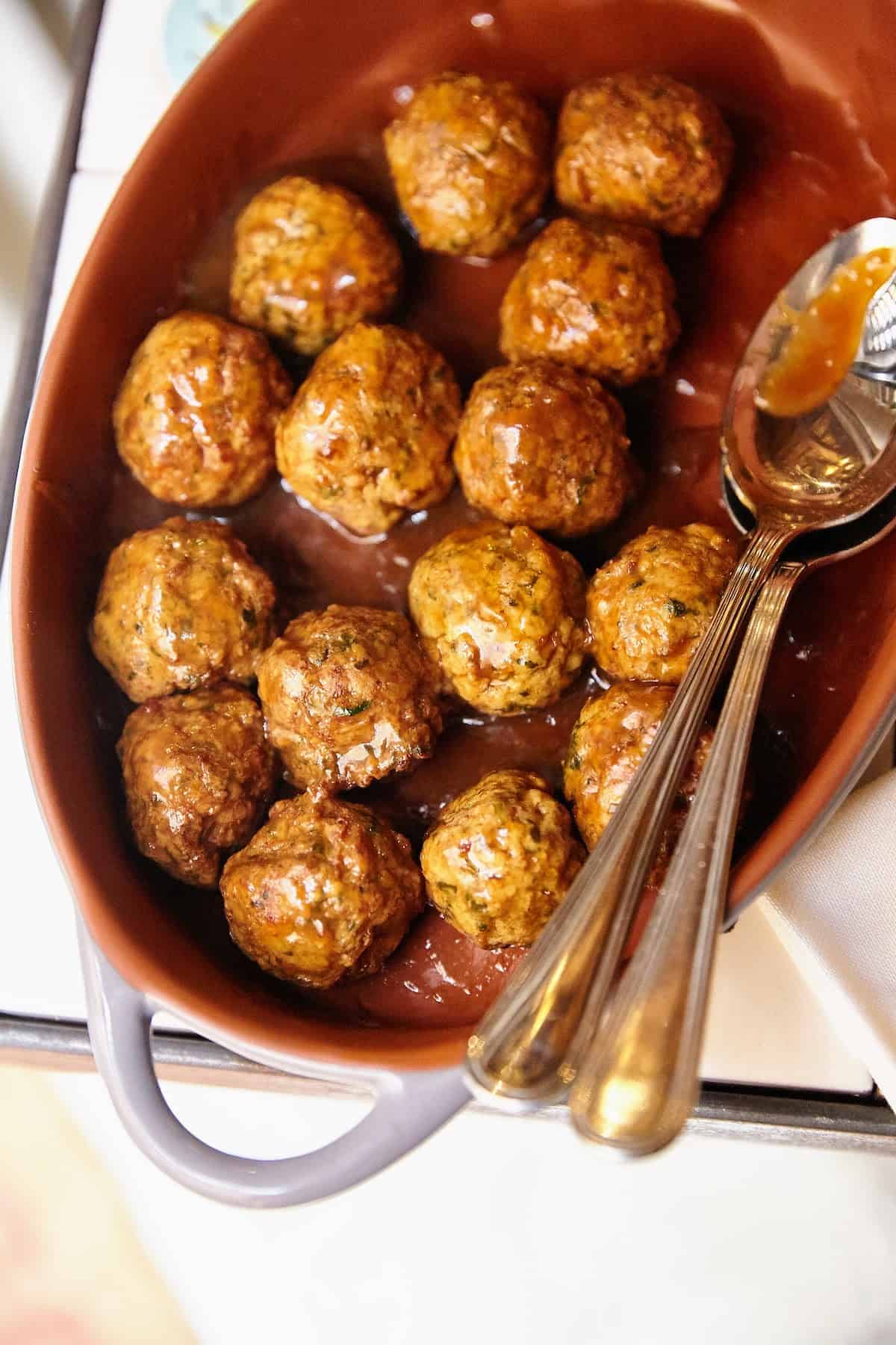 Overhead shot of saucy meatballs in a large brown serving dish.