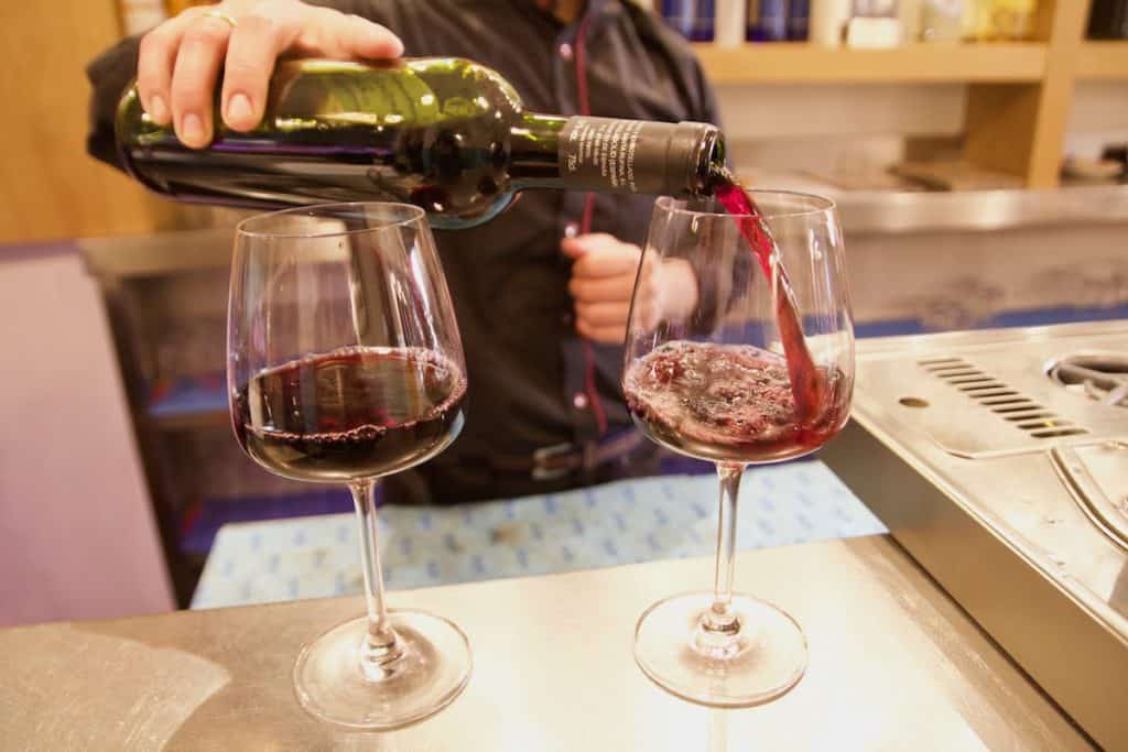 A person pouring two glasses of red wine