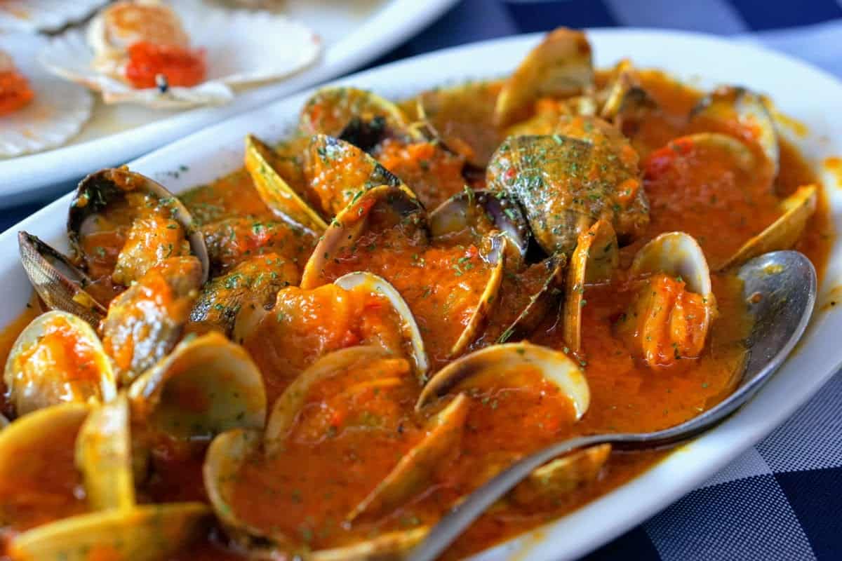 A large dish of clams covered in a bright orange sauce and herbs.