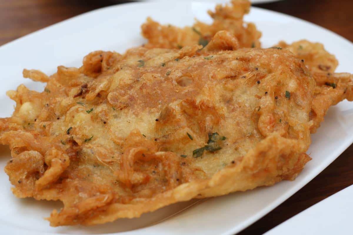 A golden brown, crispy shrimp fritter on a white plate.