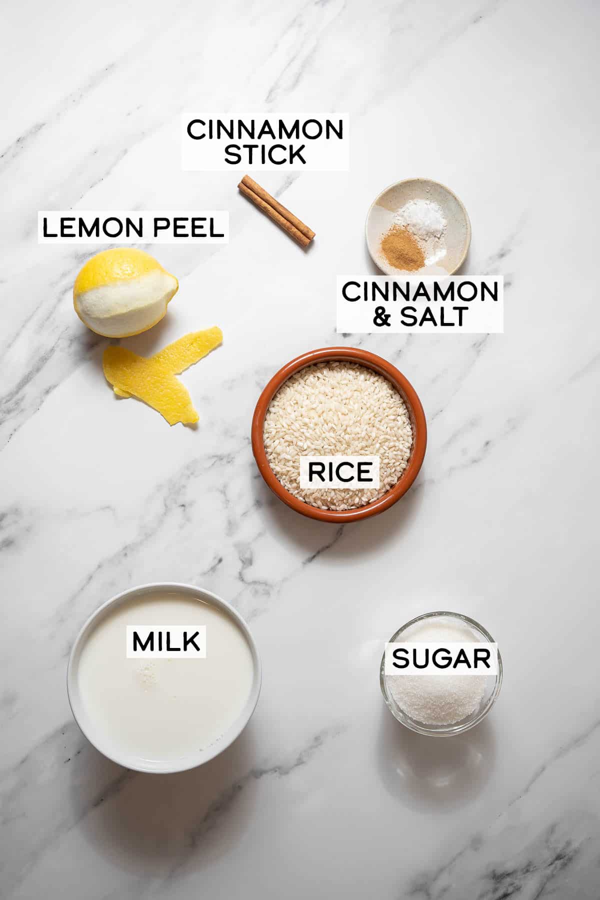 bowls of ingredients for arroz con leche on a white marble surface.