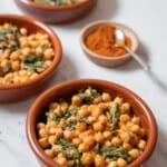 three small bowls of espinacas con garbanzo with a bowl of paprika.
