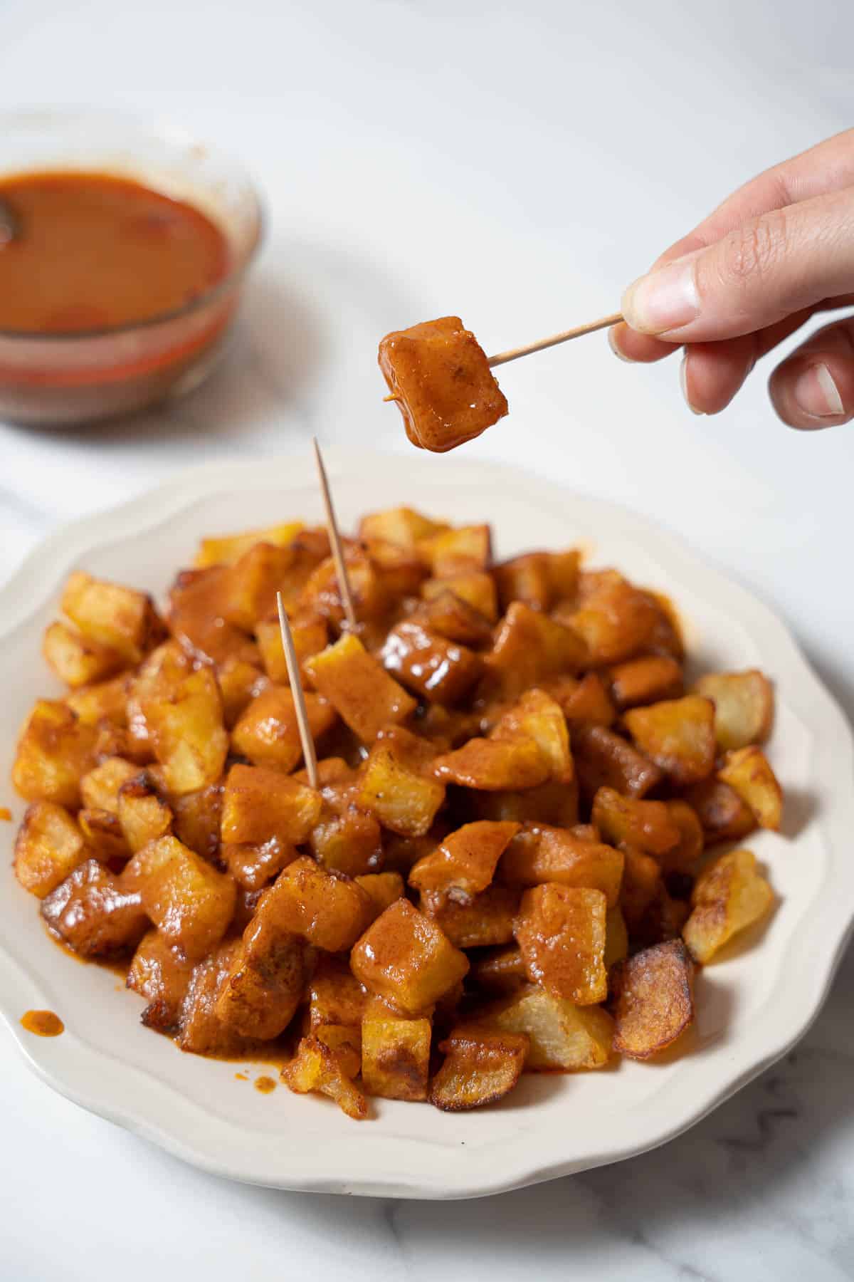 holding a patata covered in bravas sauce on a toothpick.