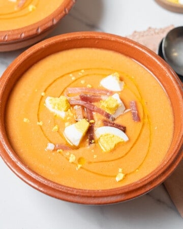 shallow bowl of salmorejo garnished with ham and boiled egg.