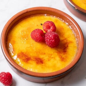 shallow dish of crema catalana garnished with raspberries.