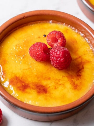 shallow dish of crema catalana garnished with raspberries.