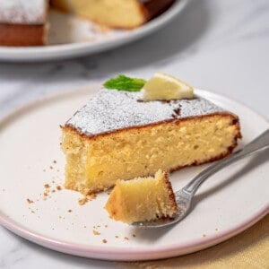 slice of lemon olive oil cake on a plate with a bite on a fork.