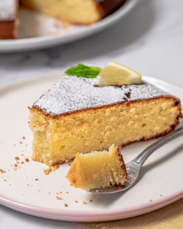 slice of lemon olive oil cake on a plate with a bite on a fork.