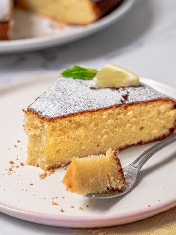 slice of lemon olive oil cake on a plate with a bite on a fork.