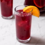 tall glass of tinto de verano garnished with an orange wedge.
