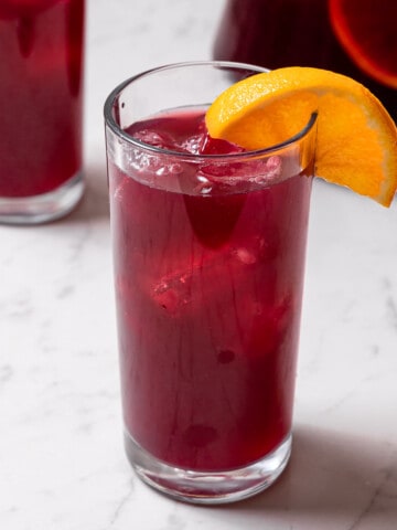 tall glass of tinto de verano garnished with an orange wedge.