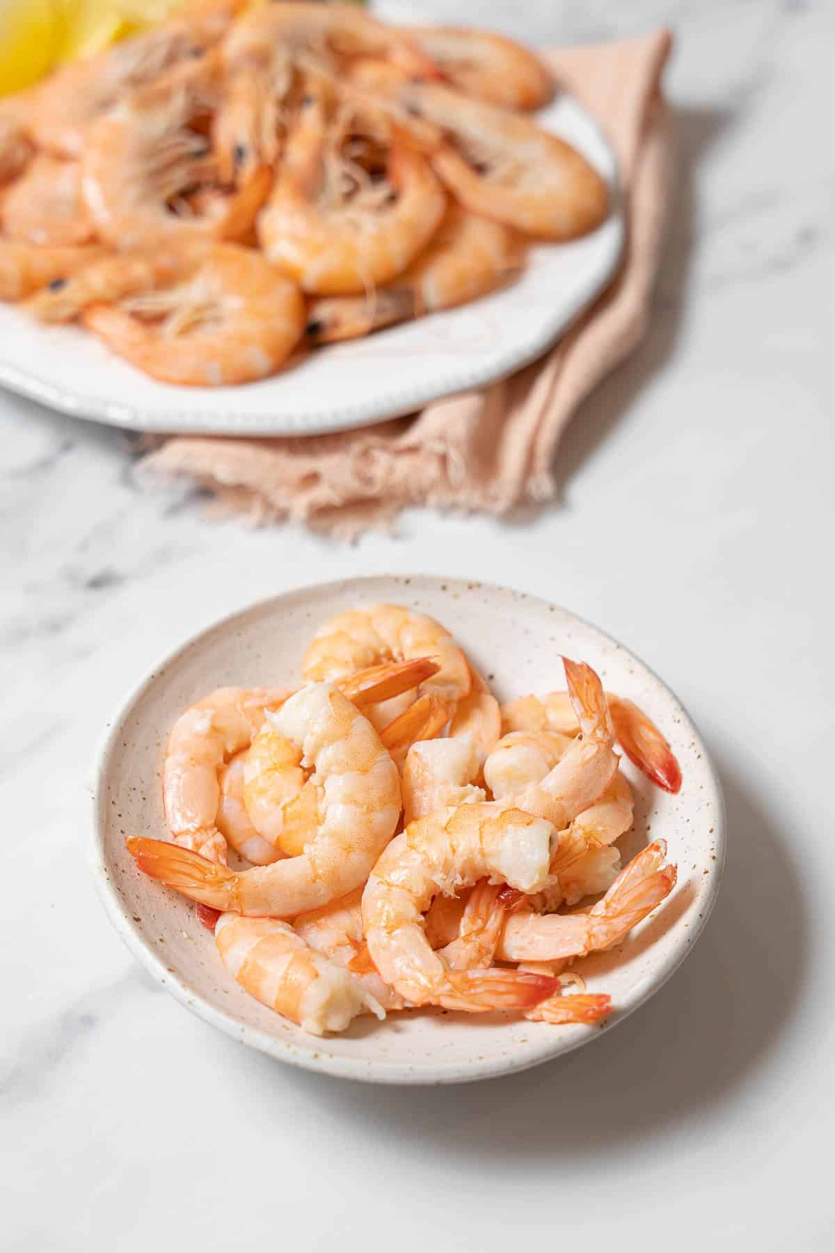 peeled boiled shrimp on a small white plate.