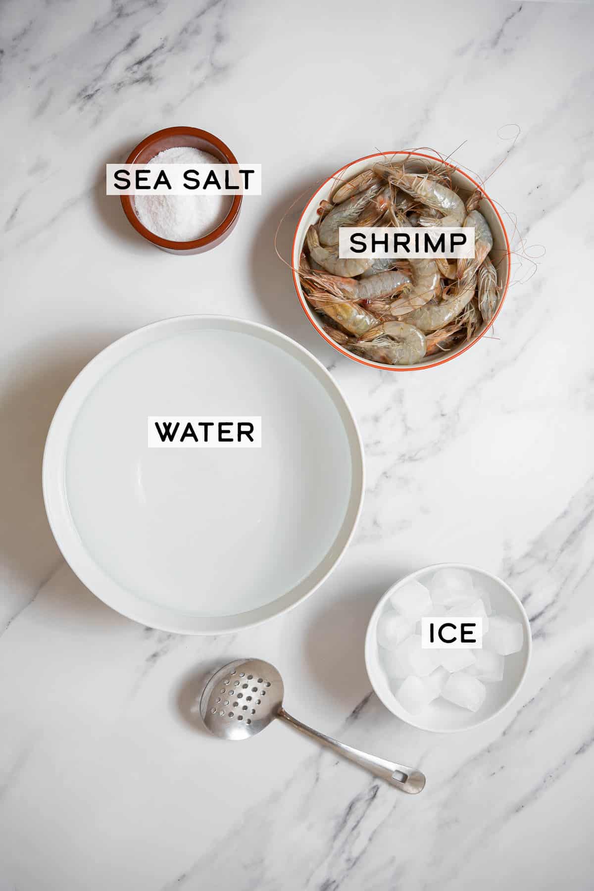 bowls of ingredients for boiled shrimp on a white marble countertop.