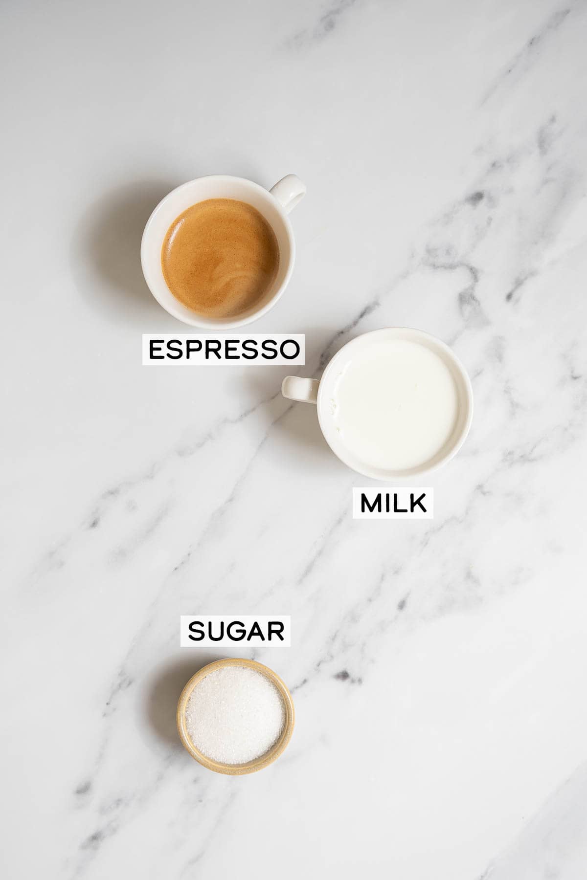 espresso, milk, and sugar on a white marble countertop.