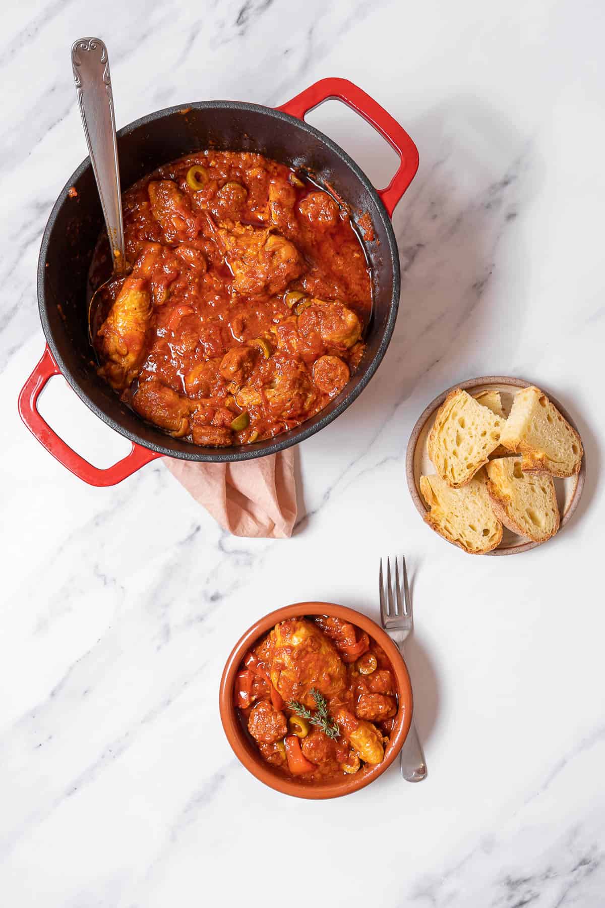 a pot of chicken and chorizo stew with a small bowl and plate of bread.
